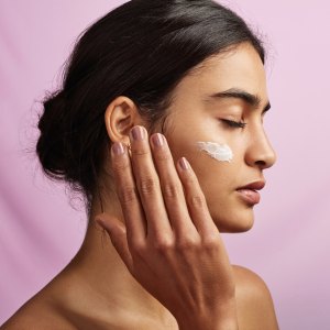 Studio shot of a beautiful young woman applying moisturizer to her face