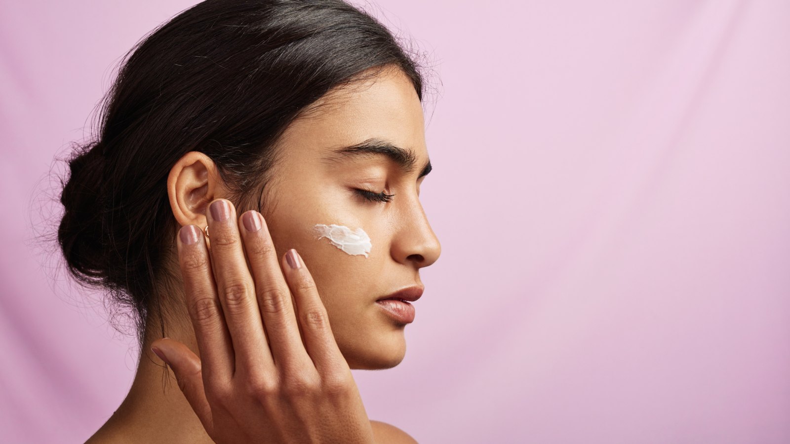 Studio shot of a beautiful young woman applying moisturizer to her face