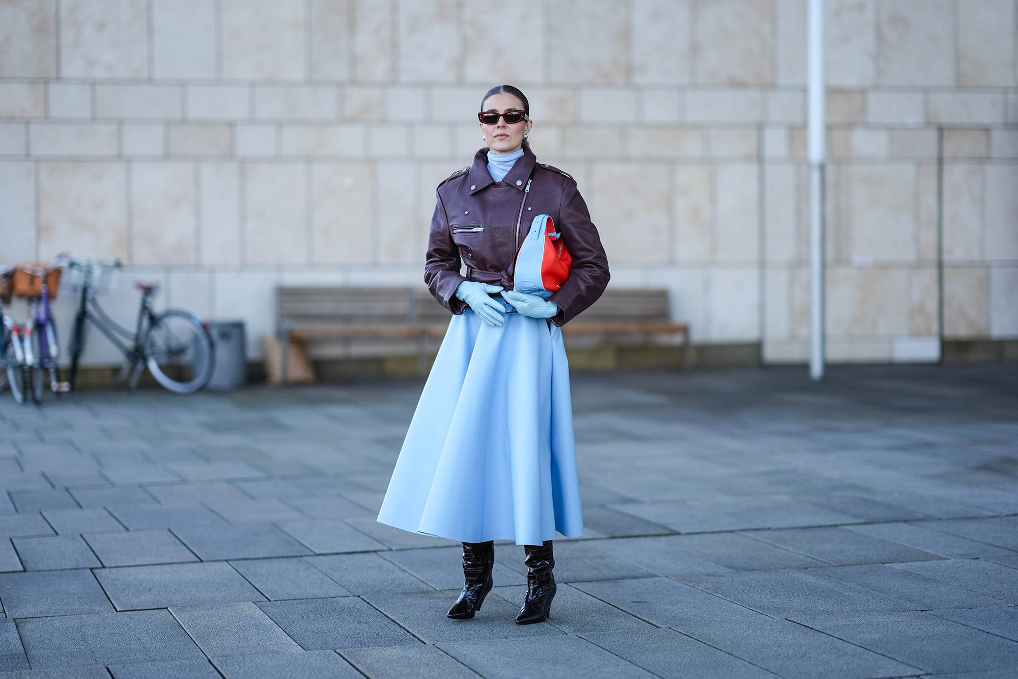 COPENHAGEN, DENMARK - JANUARY 31: Nina Suess wears sunglasses , a blue turtleneck long gathered oversized dress, a purple leather biker jacket , a red and blue bag, black leather pointed boots, outside OperaSport, during the Copenhagen Fashion Week AW24 on January 31, 2024 in Copenhagen, Denmark. (Photo by Edward Berthelot/Getty Images)
