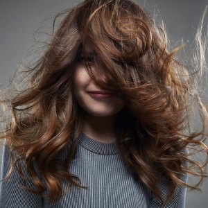 studio shot of a young female brunette in front of a gray background, wearing a gray outfit . her face half hidden behind her hair