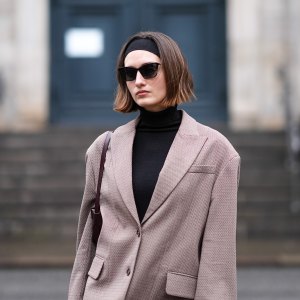 A guest wears a headband, sunglasses, a black turtleneck pullover , a beige oversized blazer jacket , outside Aeron, during the Copenhagen Fashion Week AW24 on January 30, 2024 in Copenhagen, Denmark. (Photo by Edward Berthelot/Getty Images)