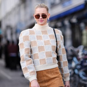 A guest wears sunglasses, a white and beige checkered / checked pattern printed turtleneck ribbed wool pullover with shoulder pads, a beige / brown suede mini skirt , outside Mark Kenly Domino Tan, during the Copenhagen Fashion Week AW24 on February 01, 2024 in Copenhagen, Denmark. (Photo by Edward Berthelot/Getty Images)