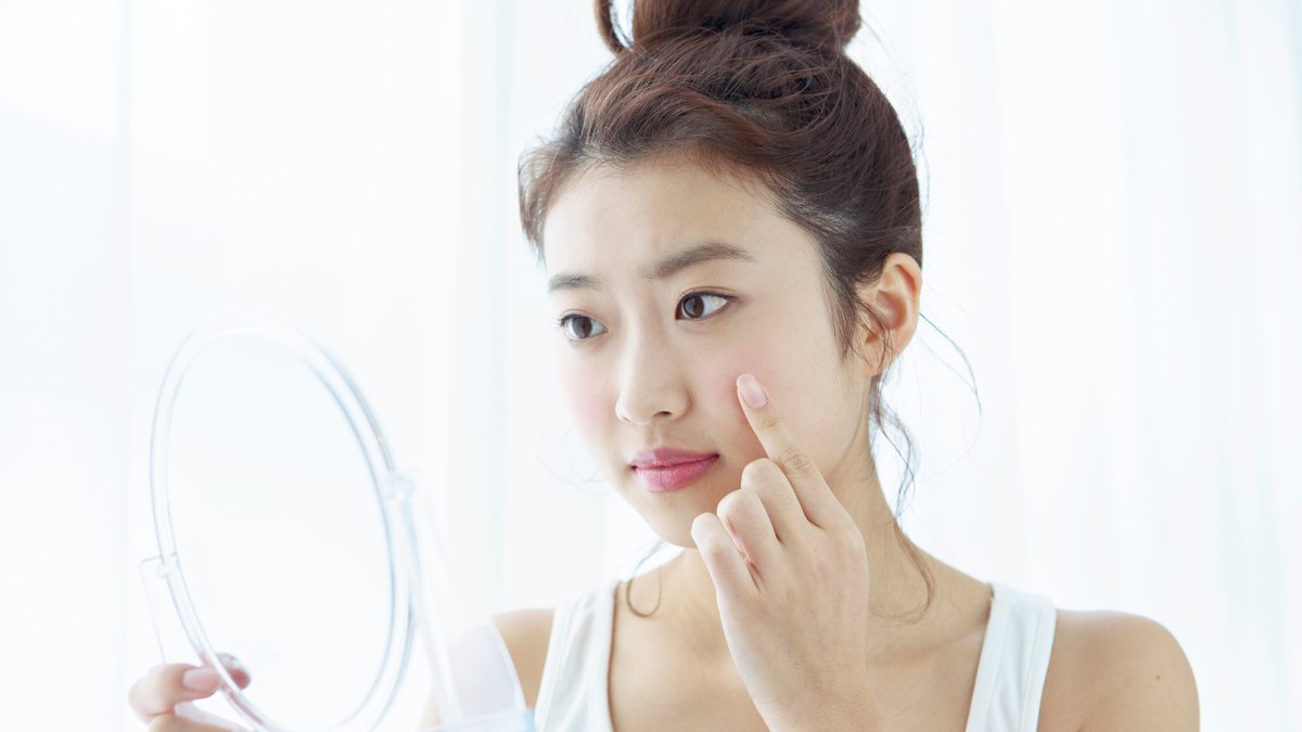 Young woman looking at her cheek in hand mirror