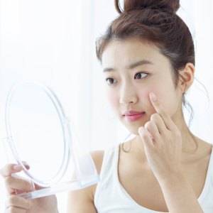 Young woman looking at her cheek in hand mirror