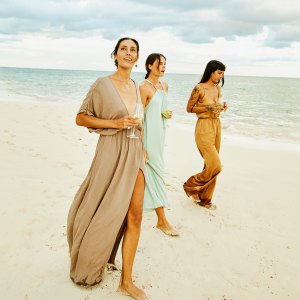 Wide shot of female friends walking on beach at tropical resort at sunset