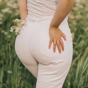 Closeup of a woman in white jeans on a blooming field background. Stylish look, fashion for curvy women, outdoor recreation.