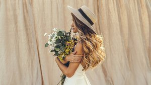 Summer lifestyle outdoors photo beautiful young woman on linen backdrop in a straw hat with field flowers