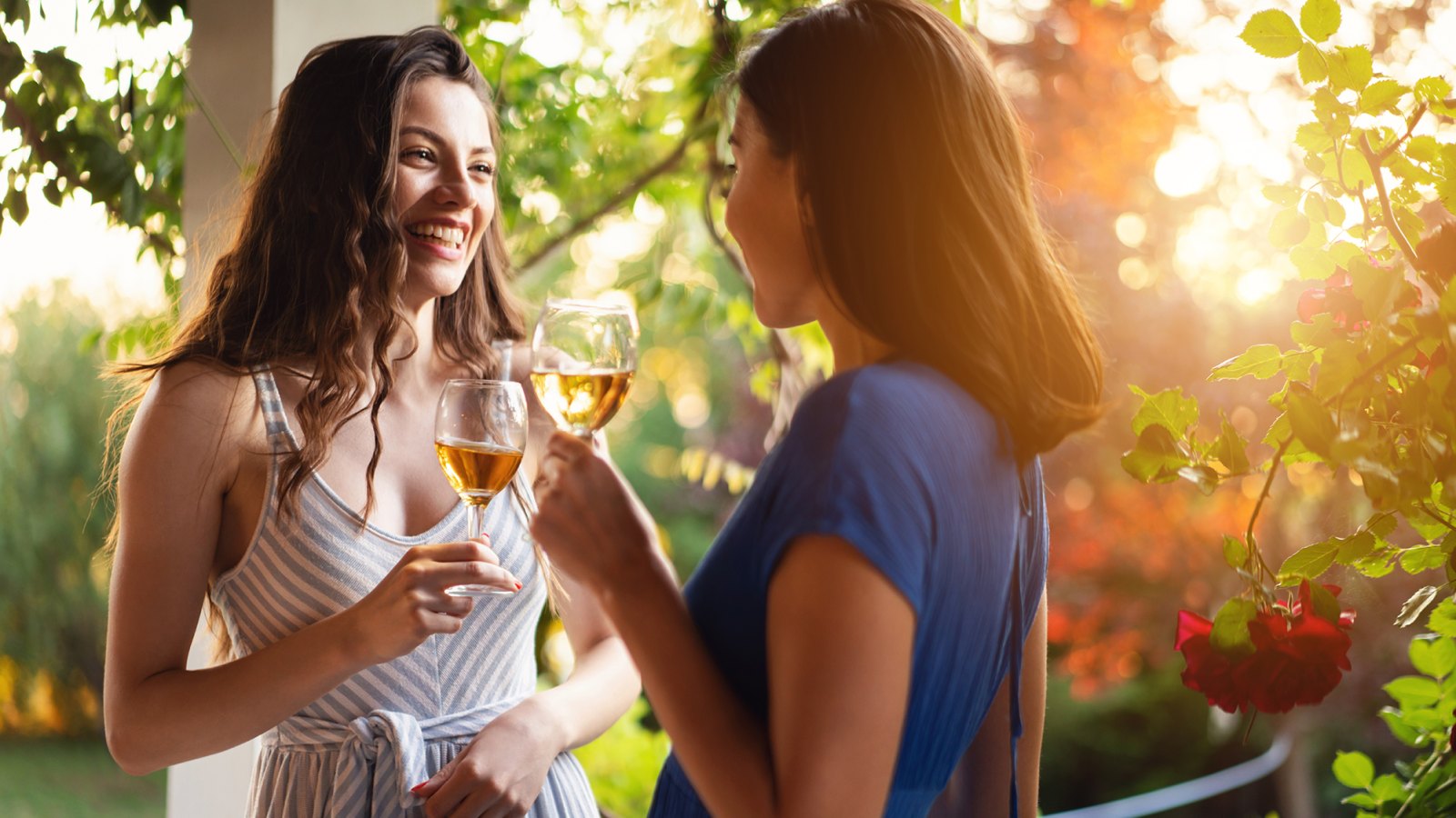 Joyful friends, drinking wine while having a casual conversation during summer garden party