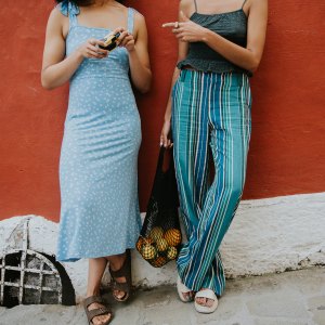 Conceptual and bright image of two females standing against a red wall in the streets of Positano. They are wearing fashionable and light clothing, appropriate for warm weather and comfortable walking sandals, perfect for exploring the winding streets of Italy.