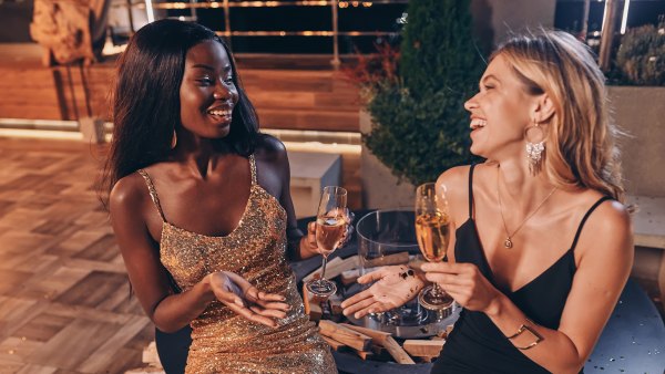 Two beautiful women in evening gowns communicating and smiling while spending time on luxury party