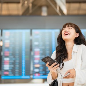 Smiling young woman text messaging on smartphone while waiting for her flight in airport lounge