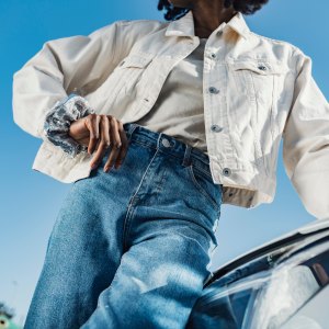 Young woman leaning on car headlight in front of sky