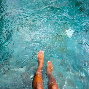 Top view of woman playing with water with legs and feet in swimming pool. Copy space. Vacation and summertime concepts.
