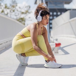 A young woman with wireless headphones tying shoelaces on her trainers before running