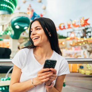 Young cheerful woman in an amusement park with a mobile phone in her hands in summer.