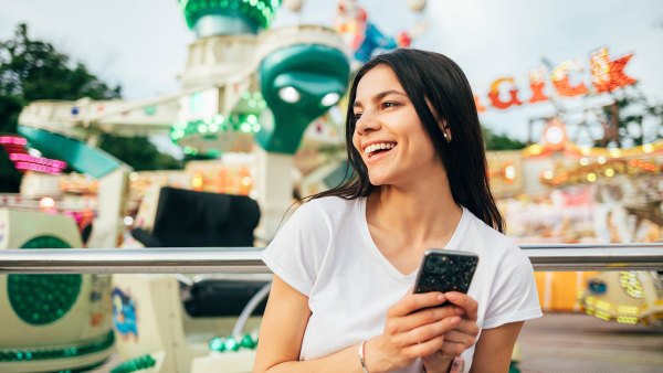 Young cheerful woman in an amusement park with a mobile phone in her hands in summer.