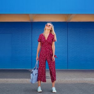Pretty blond woman wearing burgundy jumpsuit and sunglasses while walking against the blue wall and holding cerulean tote bag