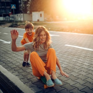 Mother and son playing in public park, driving skateboard