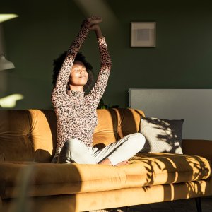 Woman with hands raised sitting on sofa at home