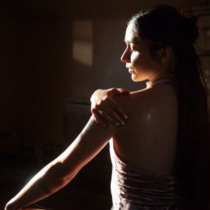 Rear view of woman applying oil to body in dark room at home