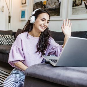 Young woman is at home, having a video call and waving at camera