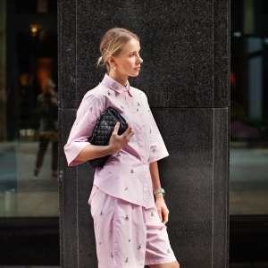 Stylish fashion woman wearing pink suit, shirt and shorts, standing confidently against a city backdrop. Urban street style allure.