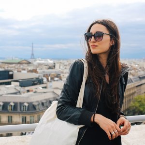 Vintage toned image of a young Parisian woman having a rest on the rooftop view in Paris, France, enjoying the view on a nice spring - early summer day. She is wearing a black leather jacket, and sunglasses, carrying a bag. Paris, lifestyle, street style fashion concepts.