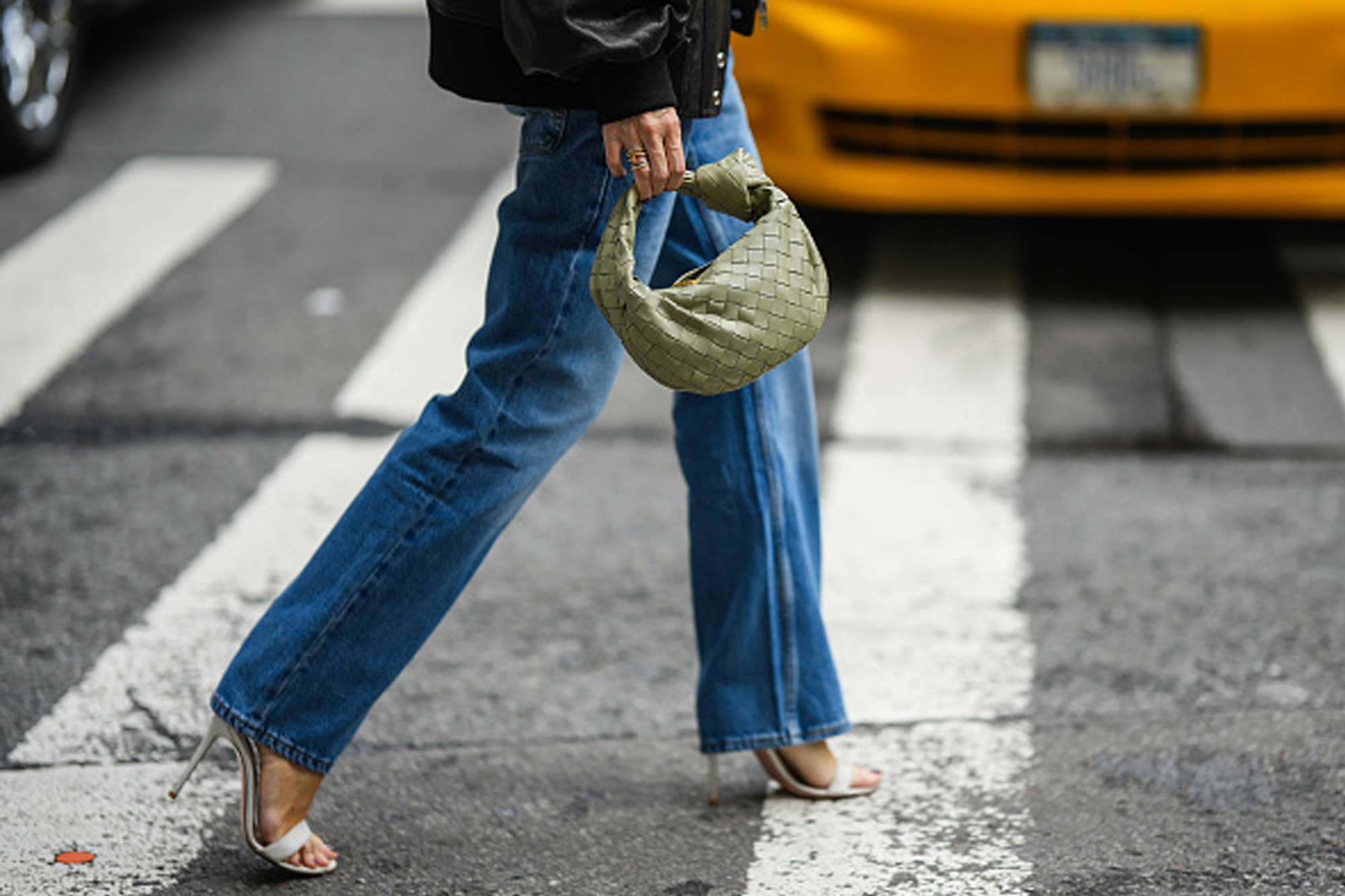woman wearing jeans, heels and purse walking across street
