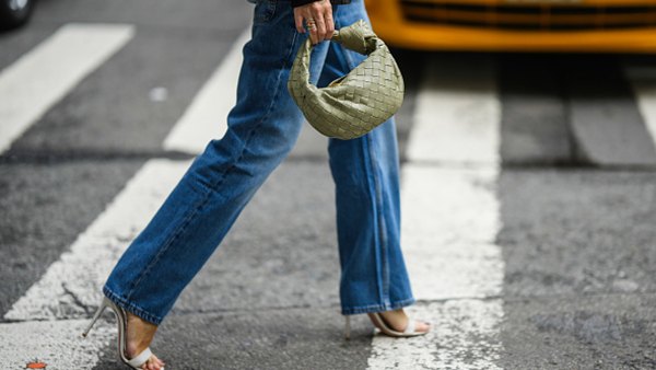 woman wearing jeans, heels and purse walking across street