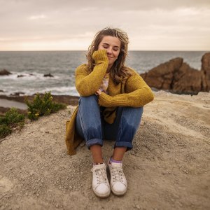 Young woman sitting and relaxing by the sea. She wears a yellow sweater and jeans