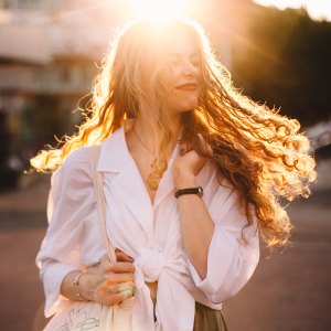 Portrait of happy successful woman with tousled hair in city at sunset