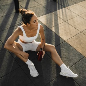 Sportive woman with slim tanned body relaxing after fitness training on outdoors sports ground. Taking a break to drink cold water and refresh. Sports hobby, healthy and active lifestyle concept.