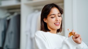 Seductive, satisfied brunette woman applying spraying perfume bottle as essential oil on the wrist