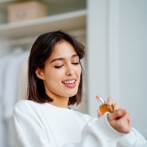 Seductive, satisfied brunette woman applying spraying perfume bottle as essential oil on the wrist