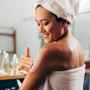 Young woman following her skin care routine, she is applying the cream after a shower.