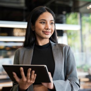 Businesswomen using a tablet while standing and looking away in a financial business office.