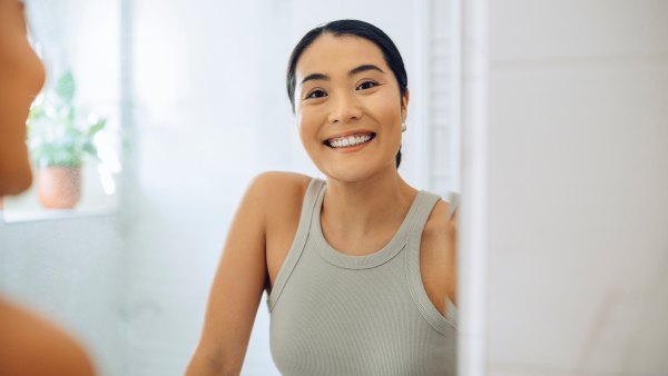 Cheerful Woman standing at her sink in the bathroom, looking at herself in the mirror.