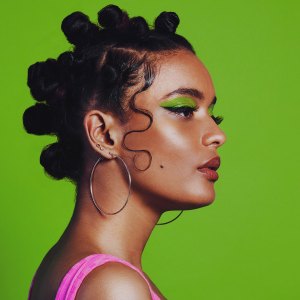 Shot of a woman posing against a green background with her bantu knots