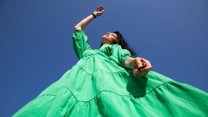 Low angle view of woman in green dress standing against clear blue sky