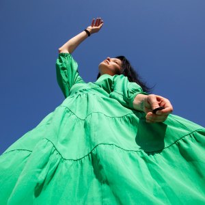 Low angle view of woman in green dress standing against clear blue sky