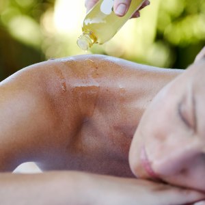 Young woman relaxing, massage oil being poured on back, close-up