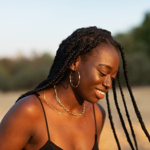 Close-up portrait of a young woman looking down while her braids move with inertia in the park at sunset