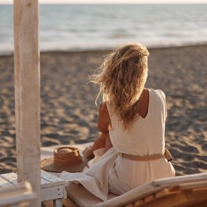 Rear view of carefree woman relaxing on a deck chair during summer day on the beach. Copy space.