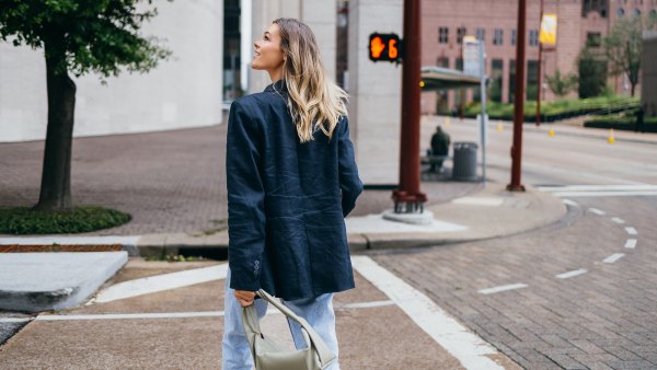Rear view of a woman walking in an urban area, looking upward. She is dressed in casual attire with a handbag.
