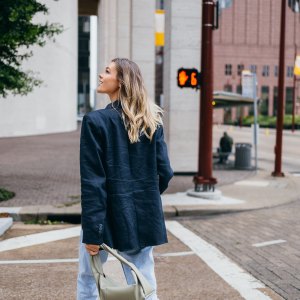 Rear view of a woman walking in an urban area, looking upward. She is dressed in casual attire with a handbag.