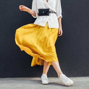 Horizontal cropped image of stylish slim woman in beautiful yellow skirt. Caucasian female fashion model standing over gray wall background outdoor with copy space.