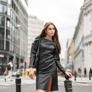 Successful beautiful business woman in fashion black clothes with a fashionable leather dress and a black trendy bag walks in a modern city