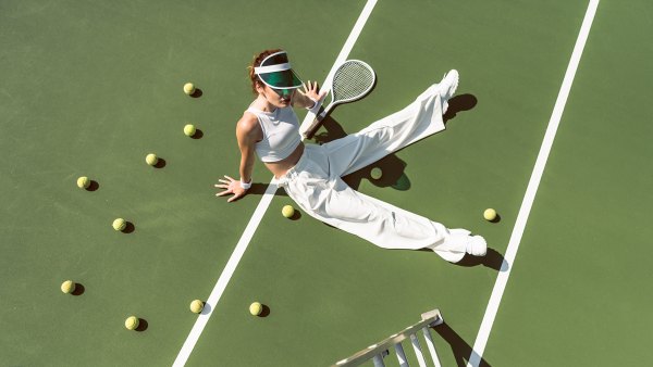high angle view of beautiful woman in stylish white clothing sitting on tennis court with balls and racket around