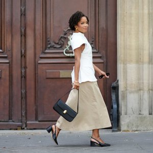 woman wearing white top, beige skirt and black bag