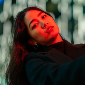 A portrait of a young woman lit by neon colored light in the city at night.